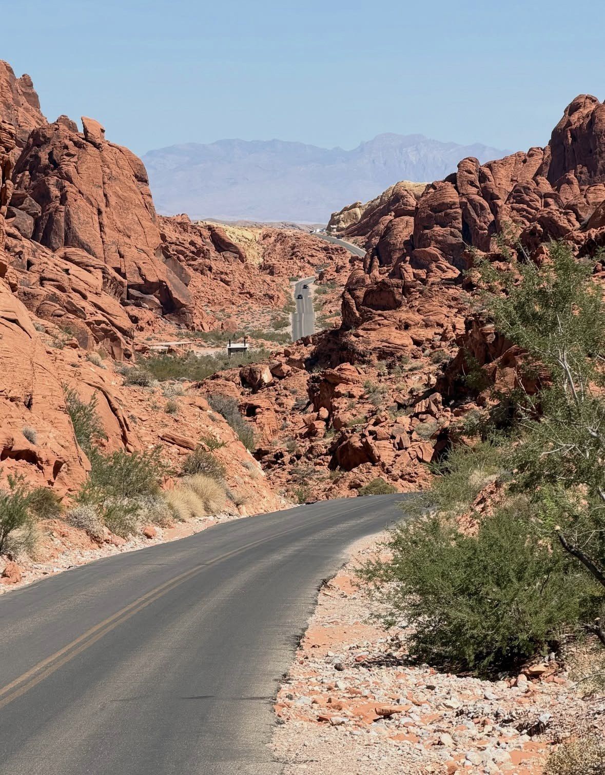 Empty asphalt road bending through red canyon walls in midday haze