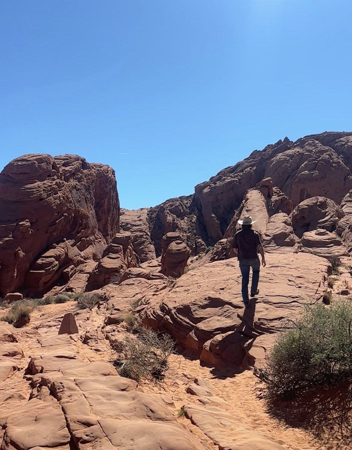 Hiker in white hat walking a slickrock ridge in bright sun