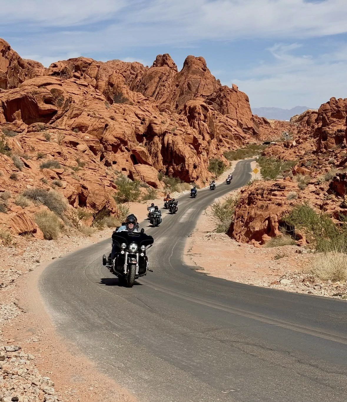 Group of motorcyclists riding the curving road past red cliffs
