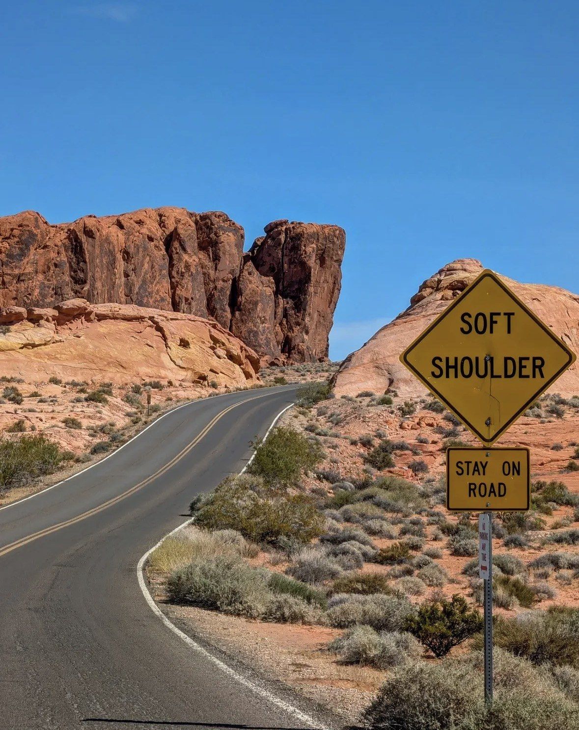 Yellow Soft Shoulder sign beside curving road and red sandstone bluff