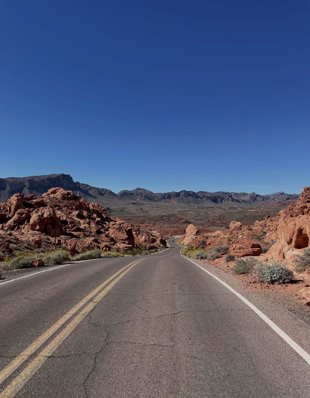 Centerline view down park road toward distant mountains, deep blue sky